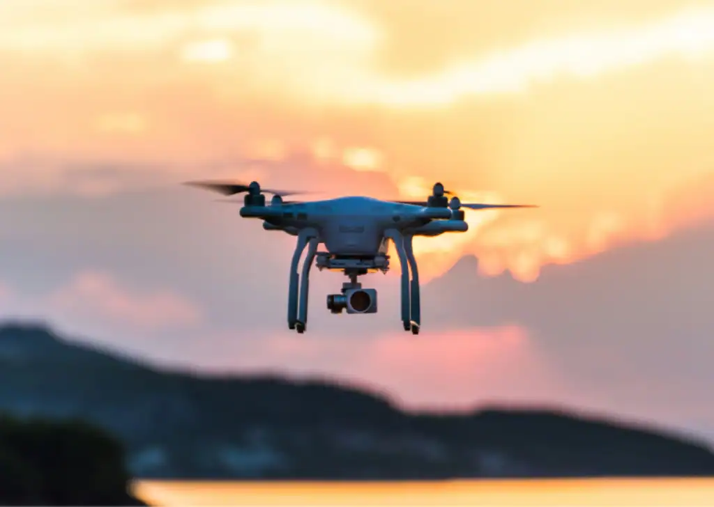 White drone hovering at sunset with mountains in background