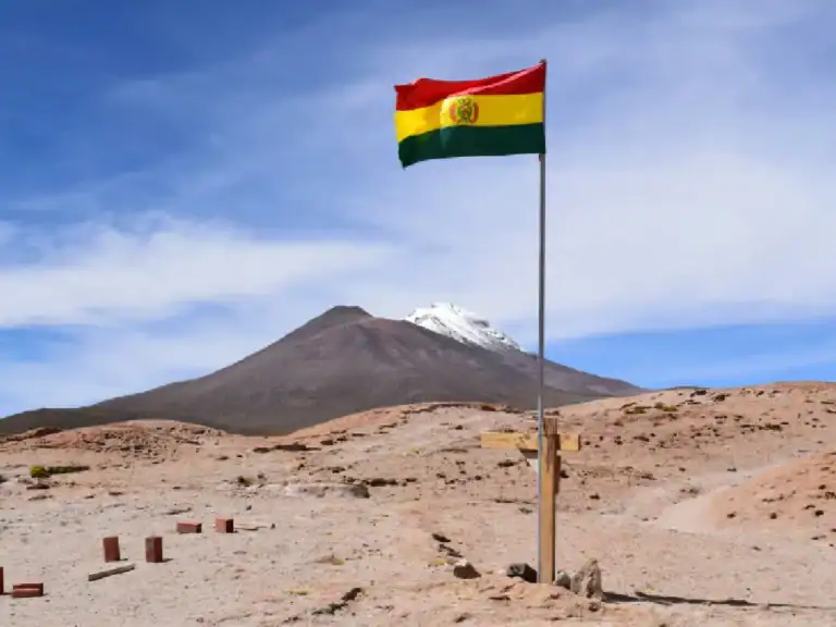 A Bolivian flag waves atop a pole in a barren, rocky landscape under a clear blue sky.