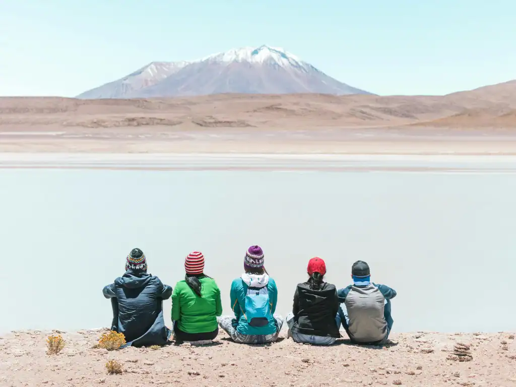 Group of travellers sitting beside a scenic lagoon with mountain views during a Bolivia backpacking trip.
