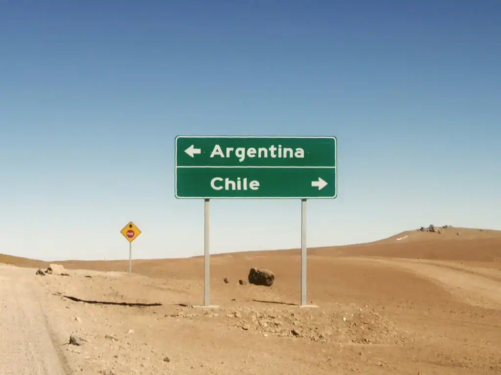 Remote desert border road with directional signs pointing towards Chile and Argentina in South America.