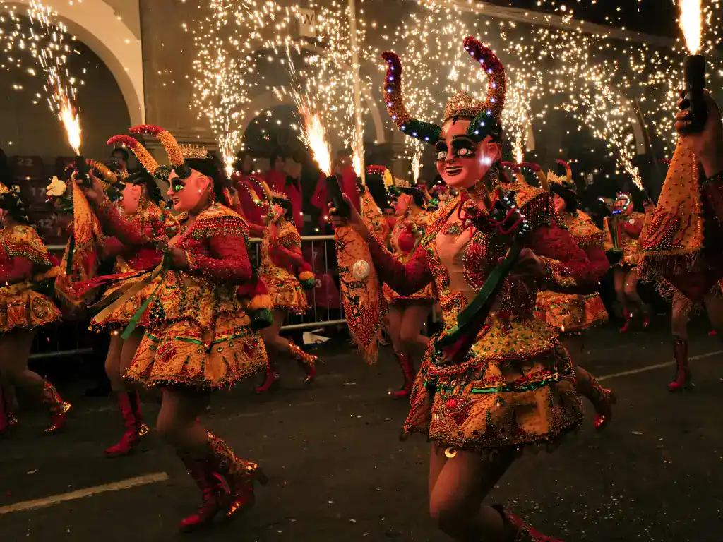 Traditional Bolivian dancers performing during a nighttime festival parade with colourful costumes, fireworks, and crowds watching.