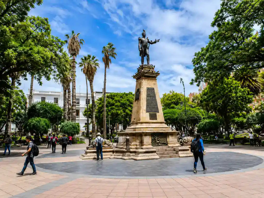 Statue at Plaza 25 de Mayo surrounded by lush gardens, palm trees and colonial architecture in central Sucre.