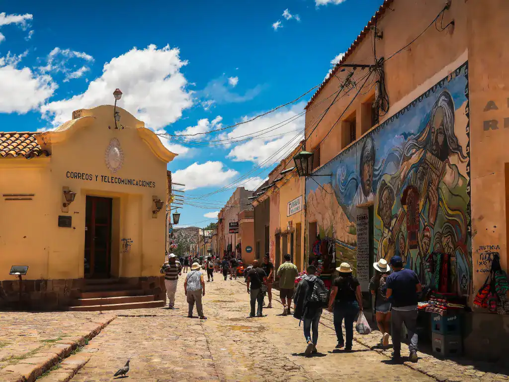 Visitors walking through a colourful colonial street in Potosí, Bolivia lined with murals and historic buildings.