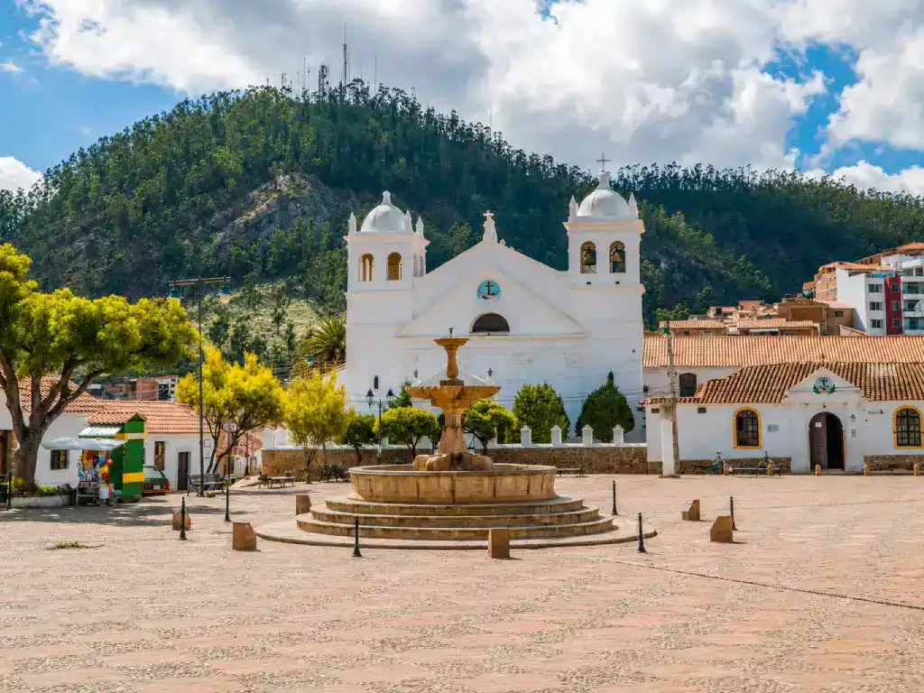 Recoleta Square in Sucre with its historic white church, central fountain and green hills rising behind the city.