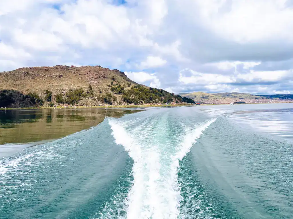 Boat cruising across the clear waters of Lake Titicaca with scenic Andean hills in the background.